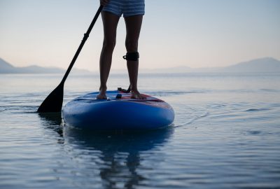 Low angle view of female legs standing on sup board floating on calm morning sea.